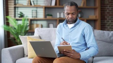 Olgun Afro-Amerikan erkek, bilgisayardaki bilgisayar ekranına bakarak internetten eğitim notlarını izliyor. Kıdemli sakallı siyah adam uzaktan öğrenmeyi dinliyor.