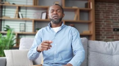 Webcam görüntüsü. Olgun Afro-Amerikan erkeği doktorla video görüşmesinde konuşuyor evdeki kanepede oturan kameraya bakıyor. Hasta kıdemli siyahi adam sorunlarını anlatıyor, hastalığından şikayet ediyor.
