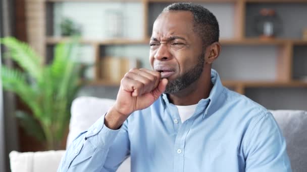 成熟的非洲裔美国人坐在客厅的沙发上咳嗽 得了感冒或流感的大胡子男性感觉很糟糕 把他的手放在胸前 他得了支气管炎 靠近点 — 图库视频影像