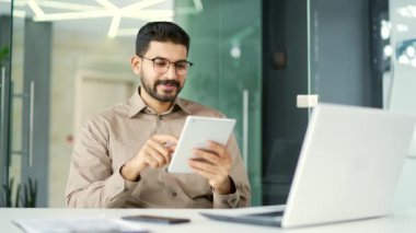 İşadamı, iş yerinde otururken dijital tablet kullanıyor. Yönetici bilgisayar uygulaması üzerinde çalışır, bir iletiyi okur, bir istemciyle sohbet eder, internette gezinir veya alışveriş yapar