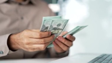 Kapatın. Erkek eller 100 dolarlık banknotları sayar. İş yerindeki iş yerindeki banknotları sayan gömlekli mutlu bir işadamı. Adam parayı elinde tutuyor. Mali başarı kavramı