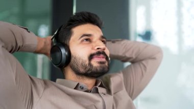 Kapatın. Kablosuz kulaklıklı sakallı iş adamı iş yerinde gözleri kapalı otururken rahatlatıcı müzik dinliyor. Mutlu girişimci rahatlama ve doğanın gürültüsünden hoşlanır.