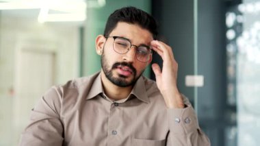 İş yerindeki iş yerinde baş ağrısından muzdarip çok çalışan sakallı iş adamı. Sinirli işçi elleriyle şakaklarına masaj yapıyor. Çok yorgun ve yüksek tansiyonu var. Kapat.