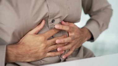 Kapatın. Erkek el, karın masajı yapıyor. Gömlekli bir iş adamı iş yerinde otururken mide ağrısı hisseder. Hasta adam şişkinlik, mide iltihabı, şişkinlik ya da spazmdan muzdarip.