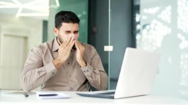 Hasta işadamı, bir iş yerinde çalışan bir dizüstü bilgisayarla çalışırken burnunun akmasından muzdarip. Üzgün erkek burnunu mendille siler. Sakallı bir adam soğuk algınlığı, virüs ya da grip olabilir.