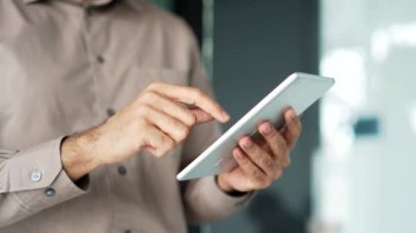 İş yerinde dijital tableti tutan erkeklerin ellerini kapatın. Tişörtlü bir işadamı bilgisayar uygulaması, okuma veya yazma üzerine çalışıyor, çevrimiçi sohbet ediyor, geziniyor, e-postaları kontrol ediyor