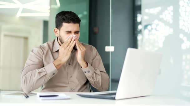 病気のビジネスマンは ビジネスオフィスの職場に座っているラップトップに取り組んでいる間 鼻水に苦しんでいます ウプセットの男性はハンカチで鼻を拭きます ひげ付きの男は風邪 ウイルスまたはインフルエンザを持っています — ストック動画