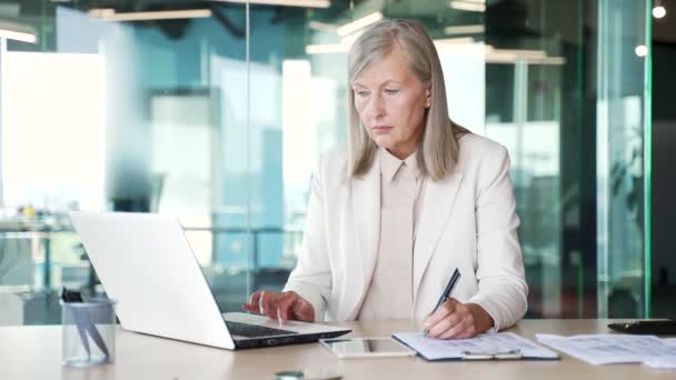 忙碌的高级灰发女商人工作时填写办公室工作场所的文件 成熟的女金融家正在使用笔记本电脑做文书工作 填写纳税申报单 — 图库视频影像