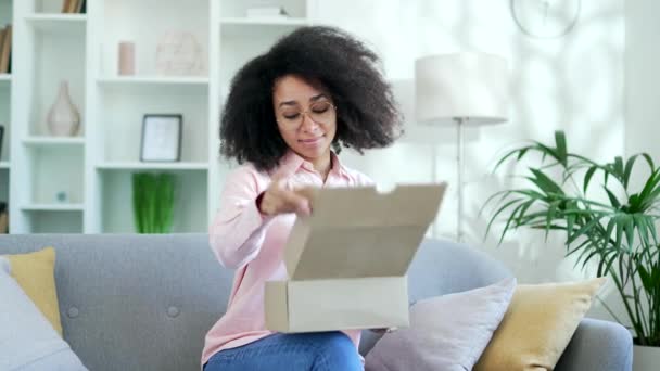 アフリカ系アメリカ人女性のお客様が自宅でパッケージを開設しました 笑顔の黒人女性バイヤーはソファーに座って購入を荷造りします Eコマースの満足するクライアント エクスプレス配送サービスのコンセプト — ストック動画