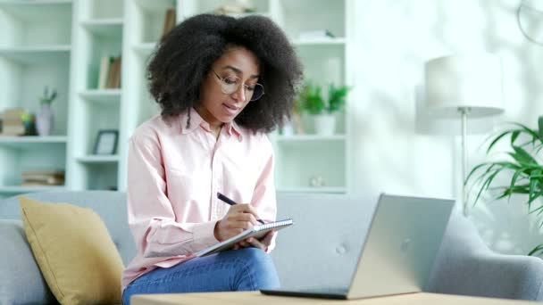 年轻的非洲裔美国女学生坐在家里听在线电子学习和视频课程 在远程学习研讨会或培训中的黑人妇女在笔记本对话中向导师写作 — 图库视频影像