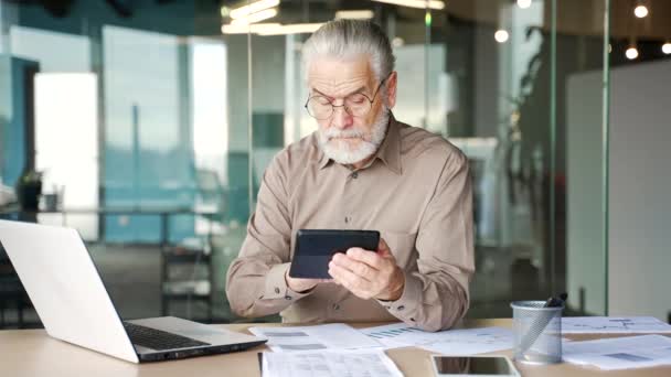 忙碌的头发灰白的大胡子商人正坐在工作场所用计算器和笔记本电脑做文书工作 在商业机构工作 进行财务计算或报税的年长业主 — 图库视频影像