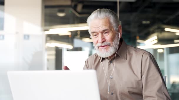 在商务办公室的一个工作场所用笔记本电脑对着电视交谈的白发苍苍的大胡子商人笑着 上了年纪的教练会说很远的话 在一次在线培训中与人交谈 靠近点 — 图库视频影像