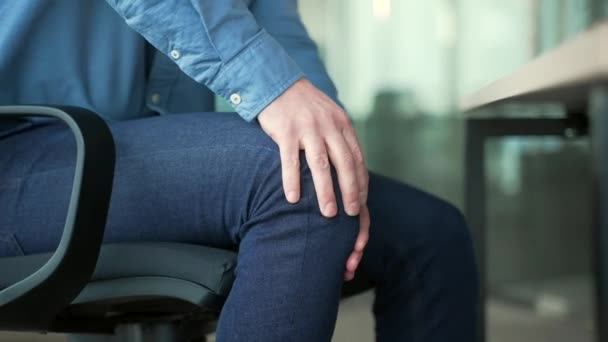 クローズアップ ビジネスオフィスで職場に座っている間 マッサージ膝を抱えている男性の手 人間は痛みを伴う膝関節痛に苦しんでいる ビジネスマンは脚の筋肉 クランプ リウマチをこすります — ストック動画