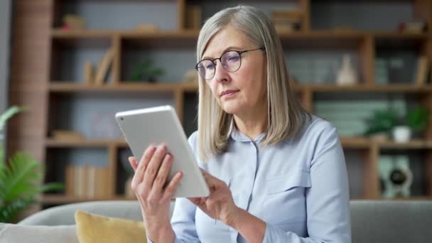 Senior Kvinna Med Grått Hår Bläddrar Digital Tablett Sitter Soffan — Stockvideo
