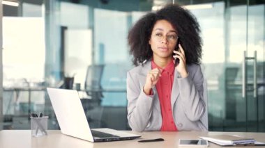 Kendine güvenen Afro-Amerikan iş kadını iş yerinde otururken telefonla konuşuyor. Meşgul siyahi kadın ya ortağıyla iş konuşur ya da müşterisiyle konuşur.