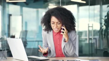 Kızgın Afro-Amerikalı iş kadını iş yerinde otururken cep telefonuyla konuşuyor. Sinirli siyahi kadın akıllı telefondaki sorunları tarif etmek için astlarıyla tartışıyor