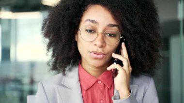 Meşgul genç Afro-Amerikan iş kadını iş yerindeki iş yerinde telefonla konuşuyor. Gülümseyen siyah kadın ya ortağıyla iş konuşur ya da müşterisiyle konuşur. Kapat.