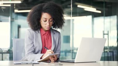 Genç afro-amerikan iş kadını video konferansını izliyor. İnternetten not alıyor. Ofiste bilgisayar ekranına bakıyor. Uzaktan eğitim alan zenci bir kadın.