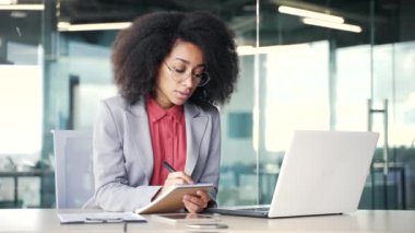 Genç afro-amerikan iş kadını video konferansı izliyor. İnternetteki konferansta dizüstü bilgisayarın ekranına bakarak notlar alıyor. Uzaktan kumandalı iş eğitimi alan siyahi bir kadın bir öğretmenle konuşuyor.