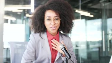 Webcam görüntüsü. Mikrofonlu genç Afrikalı Amerikalı iş kadını ofisinde oturan kameraya bakarak bir podcast kaydediyor. Kadın antrenör uzaktan eğitim veriyor, video aracılığıyla iletişim kuruyor.