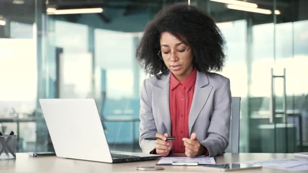 身穿西服的非洲裔美国女商人坐在办公室的工作场所用笔记本电脑对着一个视频通话 黑人妇女在网上会议上与商业伙伴进行远程交流或聊天 — 图库视频影像