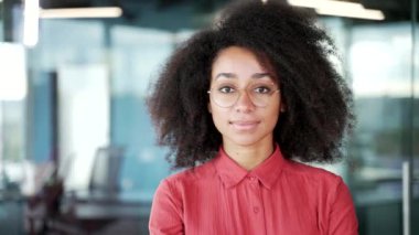 İş yerinde duran kırmızı gömlekli, mutlu, Afro-Amerikan bayan bir çalışanın portresi. Gözlüklü, gülümseyen siyah kadın kameraya bakıyor. Pozitif bir öğrencinin vesikalığı. Kapat.