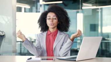 Genç Afro-Amerikan iş kadını, ofiste çalışırken gözleri kapalı meditasyon yapıyor. Siyahi kadın çalışan dizüstü bilgisayarla işe ara verdi. Sakin dişi dinleniyor, rahatlıyor, huzuru hissediyor.
