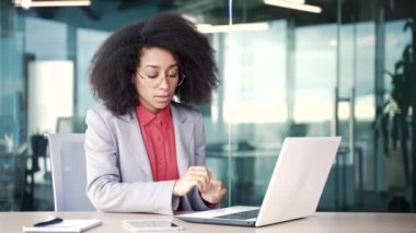 Bilek ağrısından muzdarip genç Afrikalı Amerikalı iş kadını iş yerinde laptopta çalışıyor. Zenci bir kadın esrara masaj yapıyor, elleriyle egzersiz yapıyor.