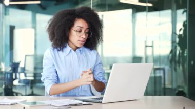 Ciddi bir Afro-Amerikan kadın çalışanı iş yerindeki bir iş yerinde dizüstü bilgisayarla video görüşmesi yapıyor. Siyahi kadın internet konferansında iletişim kuruyor ya da müşterisiyle sohbet ediyor.
