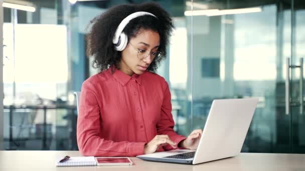 Νεαρή Αφροαμερικανίδα Ειδικός Πληροφορικής Ακουστικά Δακτυλογραφεί Φορητό Υπολογιστή Που Κάθεται — Αρχείο Βίντεο