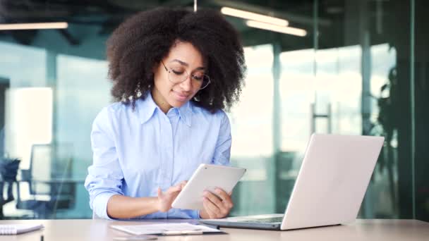 年轻的非洲裔美国女性员工正坐在办公室的工作场所使用数字平板电脑 微笑的黑人女性阅读邮件 与客户在线聊天或浏览网页 — 图库视频影像