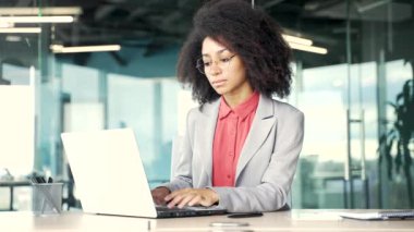 Düşünceli, konsantre olmuş, genç Afro-Amerikan iş kadını ofisteki bilgisayarında daktilo yazmayı düşünüyor. Ciddi siyahi kadın çalışanlar bilgisayar uygulamasında çalışıyor