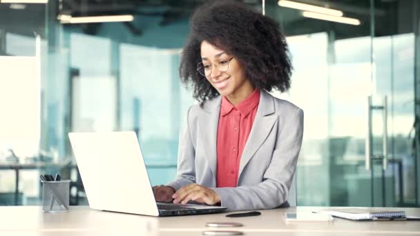 穿着夹克在笔记本电脑上打字的年轻的非洲裔美国女商人坐在办公室的工作场所 从事计算机应用 银行业务 发短信 网上聊天的黑人妇女 — 图库视频影像