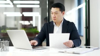 Mutlu Asyalı işadamı, iş ofisinde oturan dizüstü bilgisayarında incelediği mali raporun sonuçlarından memnun. Olgun adam belgelere olumlu göstergelerle bakıyor