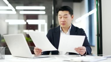 Kafası karışmış Asyalı işadamı iş yerindeki evrak işlerinde zorlanıyormuş. Resmi takım elbiseli, kafası karışmış olgun bir adam belgelere bakıyor ve sorunu anlayamıyor.