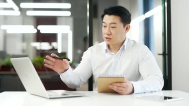 Asyalı işadamı bilgisayardaki konferans notlarını izliyor. Ofiste oturan dizüstü bilgisayara bakıyor. Uzak bir iş toplantısı ya da eğitimi olan bir adam, özel öğretmeniyle konuşur.