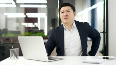 İş yerindeki bilgisayarında çalışırken sırt ağrısı çeken Asyalı iş adamı hasta, takım elbiseli olgun bir adam sırt kası spazmları geçirir, sırtına masaj yapar,