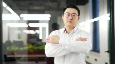 İş yerinde kollarını kavuşturmuş duran ciddi bir Asyalı müdürün portresi. Gözlüklü ve gömlekli kendinden emin bir adam kameraya bakıyor. Bir iş adamının kafasından. Boşluğu kopyala