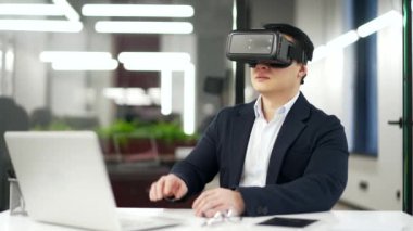 Resmi takım elbiseli Asyalı işadamı sanal gerçeklik simülatöründe sanal gerçeklik gözlüğü kullanıyor. Yönetici bilgisayar programlarını kontrol etmek ve sanal sayfaları çevirmek için jestler kullanır