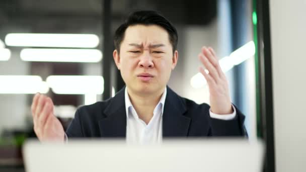 ストレスを受けたアジアのビジネスマンは ビジネスオフィスの職場に座っている間 ノートパソコンで悪いニュースを読みます フォーマルなスーツの男性が コンピュータにネガティブなメッセージを受け取ったことにショックを受けた クローズアップ — ストック動画