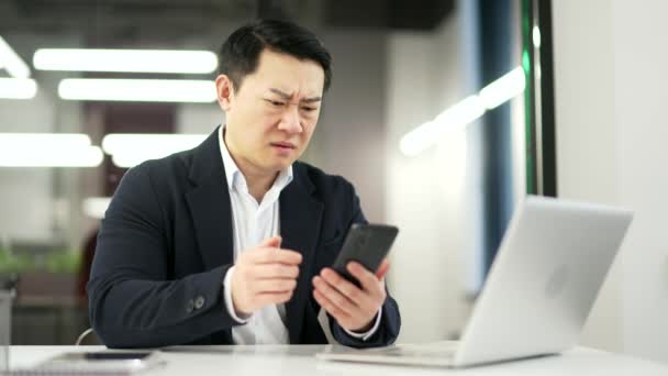Frustrovaný Stresovaný Asijský Podnikatel Čte Špatné Zprávy Smartphonu Zatímco Sedí — Stock video