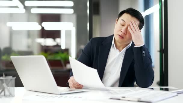 勤勉なアジアのビジネスマンは ビジネスオフィスの職場に座って書類ワークをすることに疲れています 正式なスーツを着た成熟した男性は過剰になり 退屈です 過負荷の排出された金融業者は仕事で困難があります — ストック動画