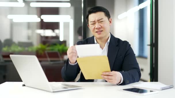 アジアのビジネスマンは ビジネスオフィスの職場でデスクに座っている悪いニュースで手紙を読んで心配しました 不快な通知を受けたことにイライラした正式なスーツで起業家を失望させた — ストック動画