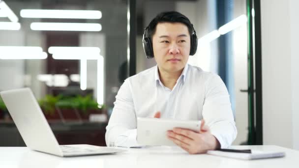Happy Asian Businessman Wearing Wireless Headphones Listening Music Sitting Desk — Stock Video