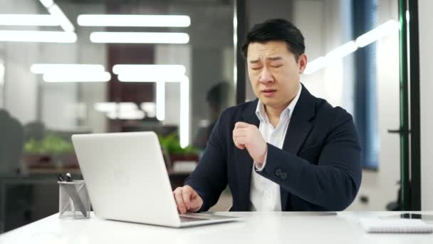 アレルギー性のアジアの男は ハンカチで鼻をくしゃみ 拭きます ビジネスオフィスのデスクに座っている間 季節のアレルギーに苦しむ正式なスーツで成熟したビジネスマン — ストック動画