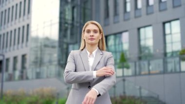 Bir ofis binasının yanında caddede duran mutlu bir iş kadınının portresi. Resmi takım elbiseli, kollarını kavuşturup kameraya bakan gülümseyen bir kadın. Pozitif kadın girişimcinin vesikalığı