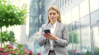 Gülümseyen bir işadamı caddede bir ofis binasının yanında telefon kullanıyor. Resmi takım elbiseli mutlu olgun bayan yönetici müşteriyle mesajlaşan ya da internette gezinen bir mesaj yazar.