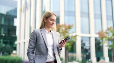 Gülümseyen bir işadamı bir ofis binasının yakınında yürürken bir telefon kullanıyor. Resmi bir takım elbise içinde mutlu olgun bir kadın mesajlaşan, mesajlaşan, mesajlaşan, e-postaları kontrol eden ya da internette gezinen