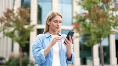 Üzgün kadın, modern bir binanın yanında caddede dikilirken telefonda kötü haberler okuyor. Hüsrana uğramış olgun bir kadın nahoş bir haber aldı ve endişeli bir şekilde akıllı telefondan istenmeyen mesajlara baktı.