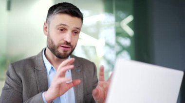 Ofisteki iş yerinde dizüstü bilgisayarla konuşan kendine güvenen bir iş adamı. İşçi bir adamın iş görüşmesi var, uzaktan konuşuyor, çevrimiçi konferansta iletişim kuruyor. Kapat.